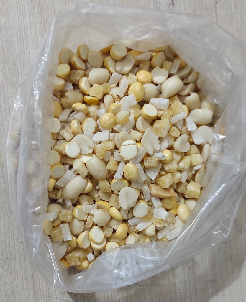 A transparent bag filled with a mixture of yellow and white snacks and sweet ingredients, commonly used in traditional Indian sweets.